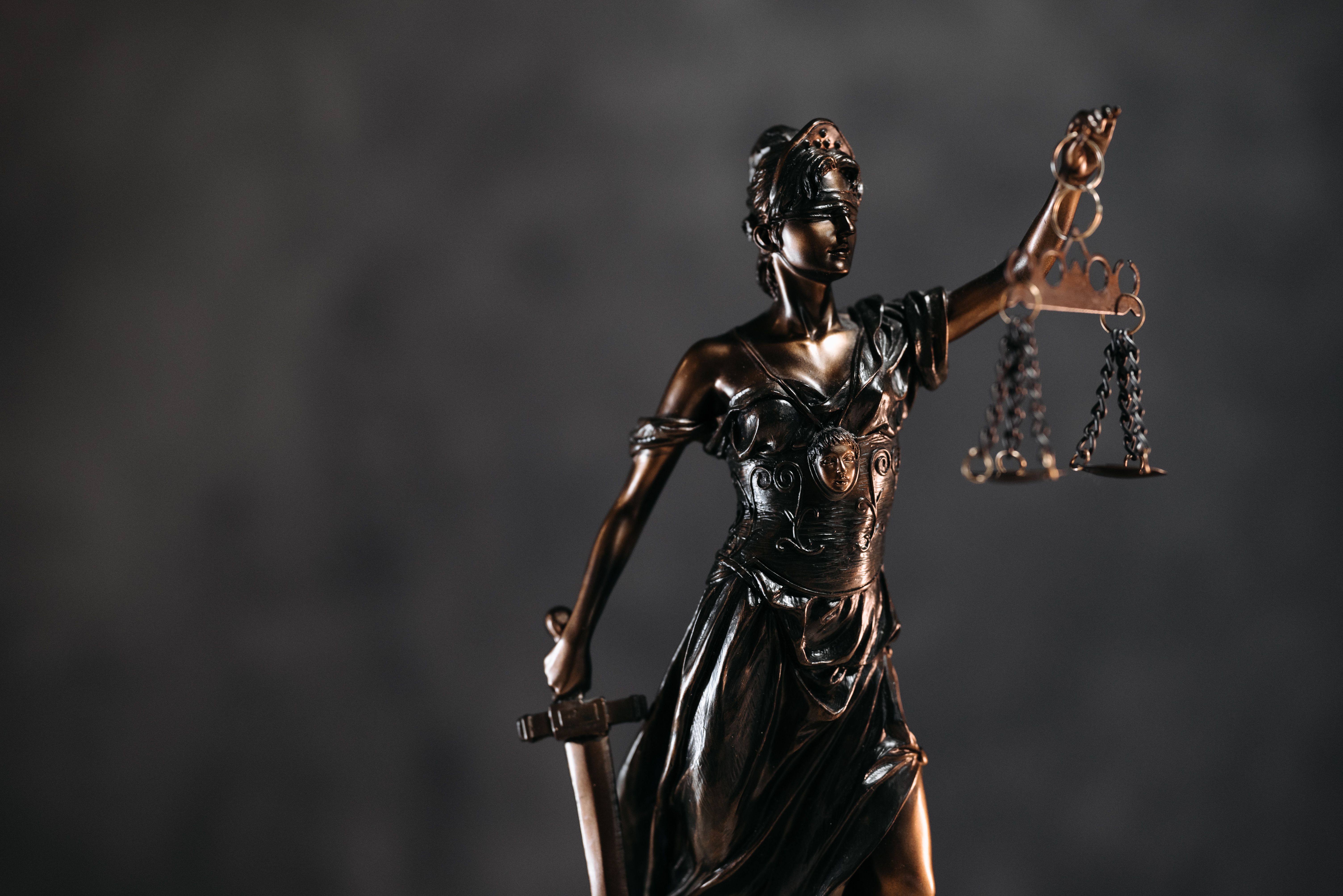 Detailed bronze Lady Justice statue holding scales and a sword against a dark background