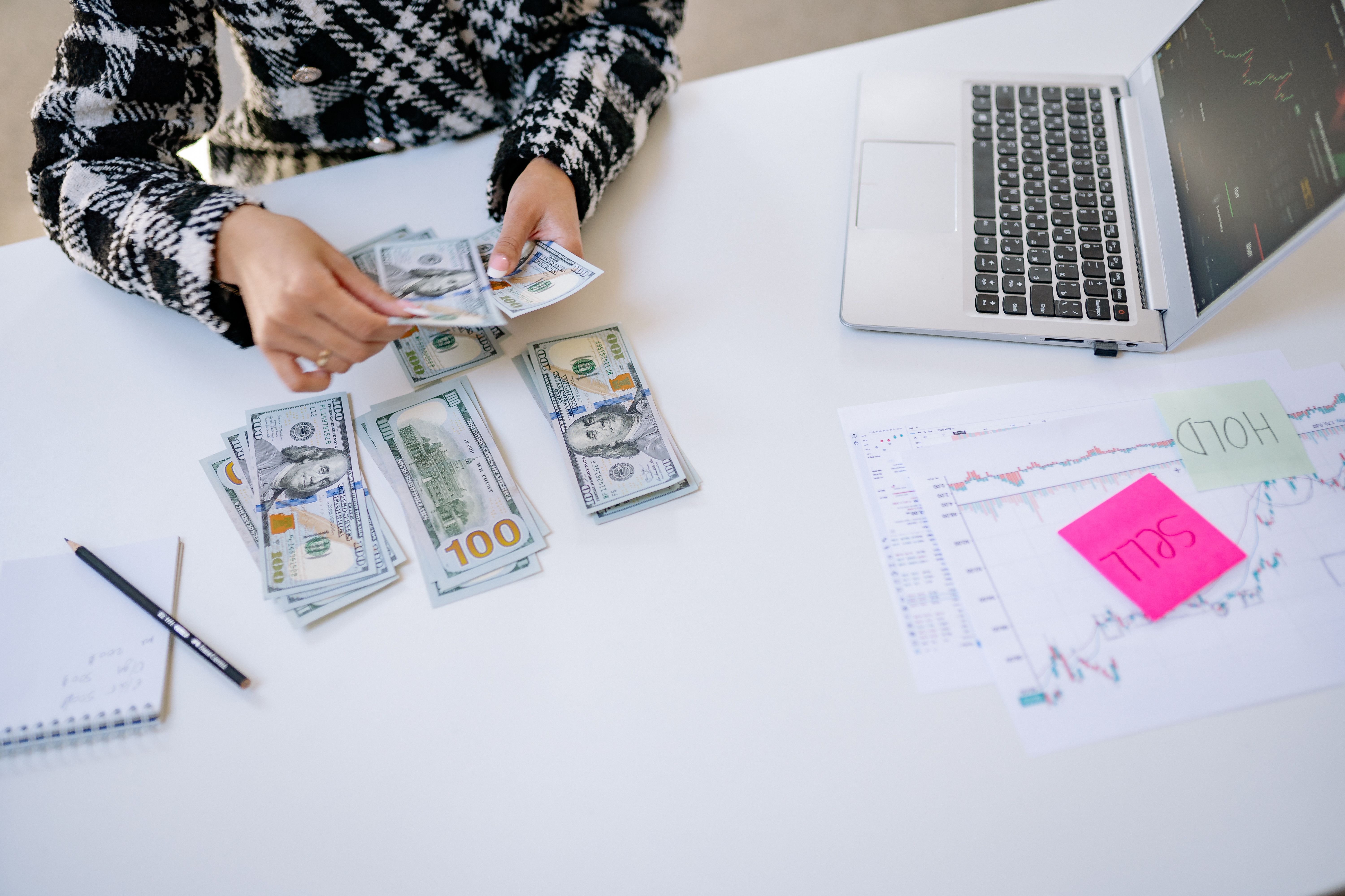 Person counting cash next to a laptop and stock market charts representing litigation finance and investment returns