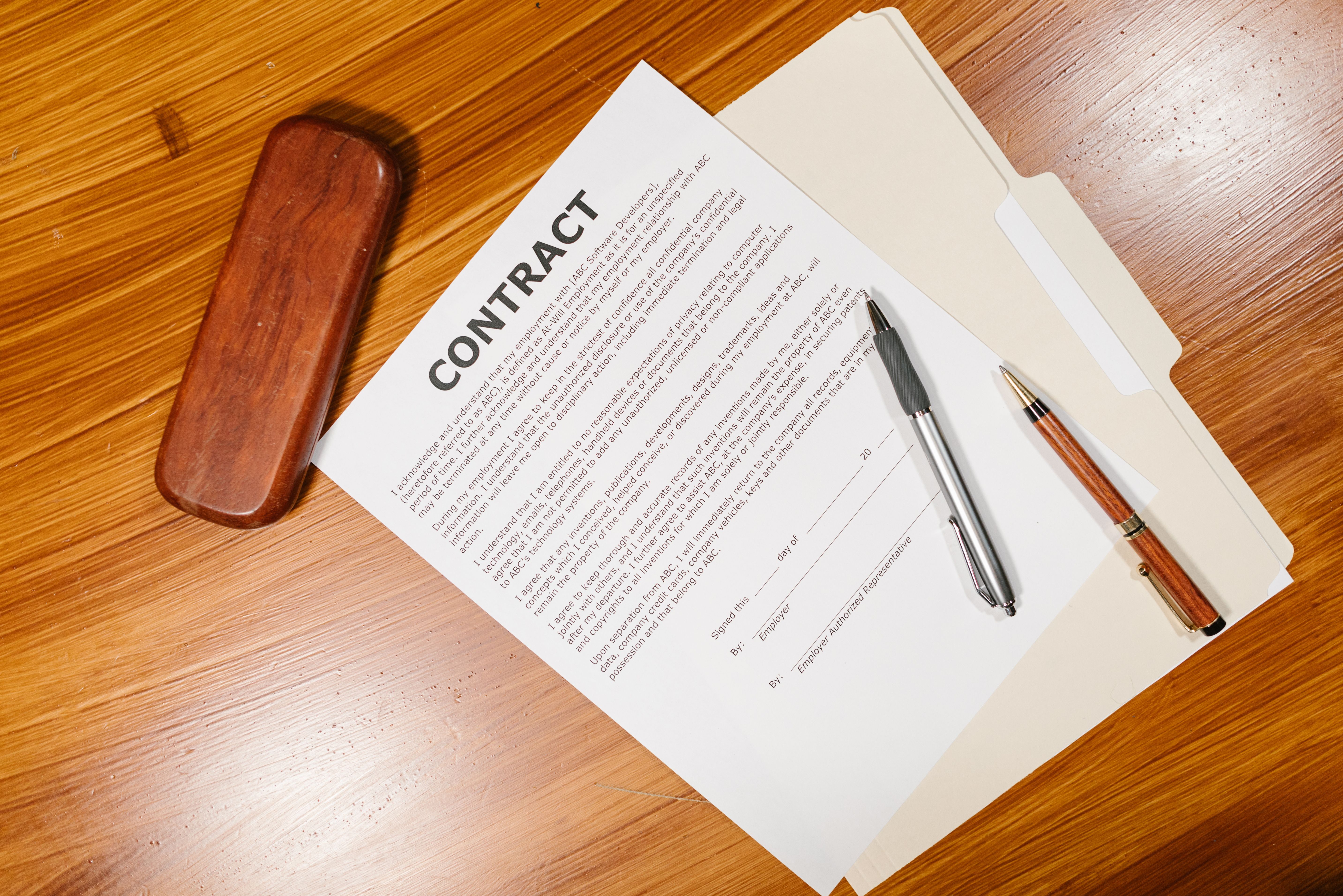 High-angle view of contract documents, pens and a case on a wooden table representing litigation paperwork