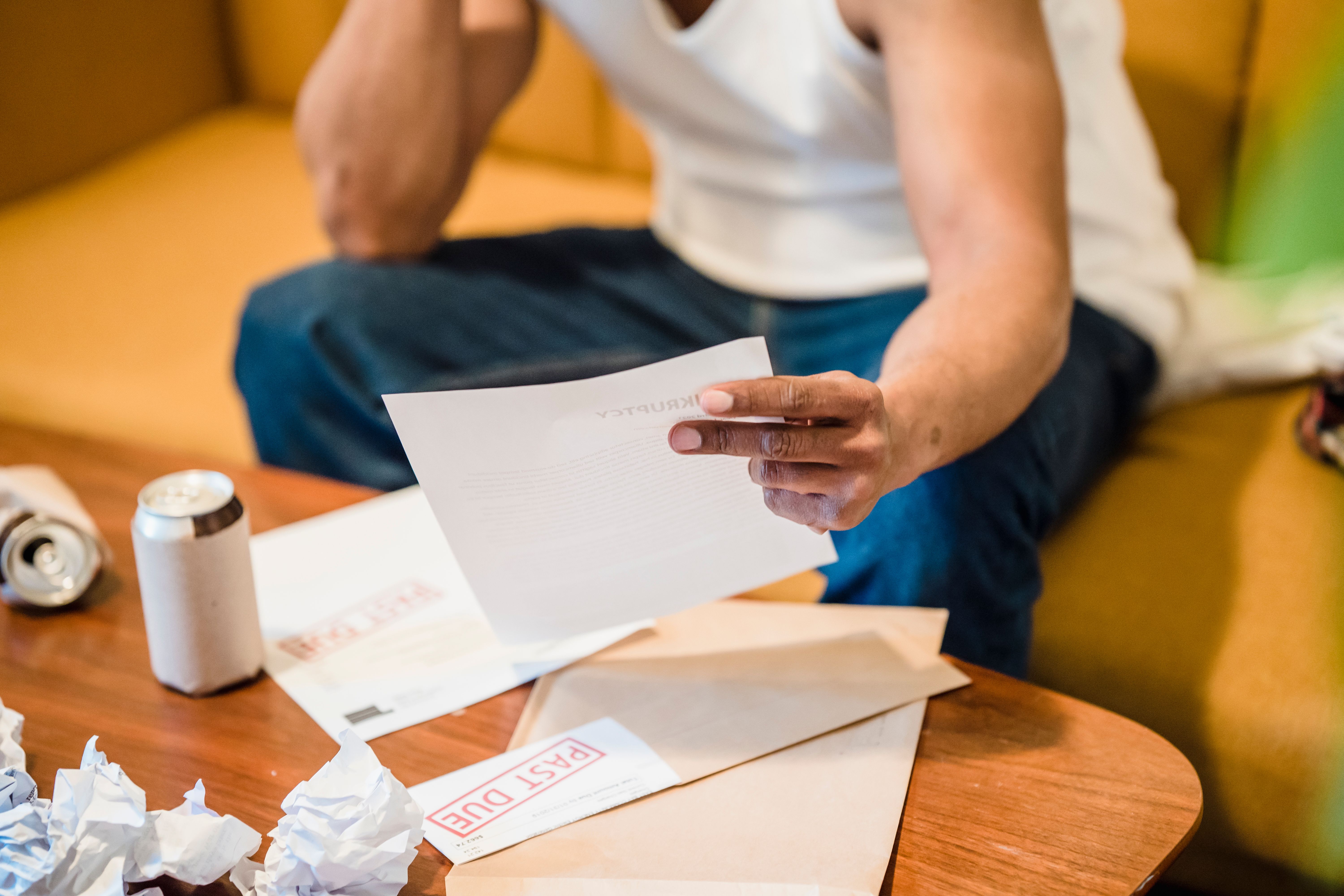 Man reading unpaid bills while feeling stressed about legal and household debt.